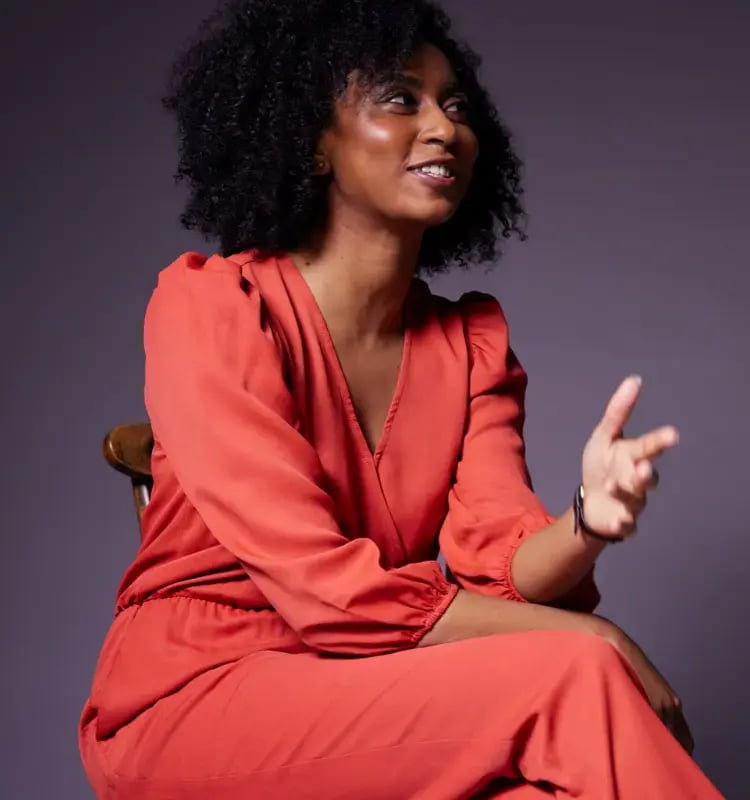 Black woman in a red dress sat in a wooden chair and looking up smiling