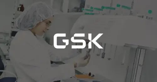 Photo of a woman in a lab coat and protective equipment holding a vile up to a digital machine and a white version of the GSK logo superimposed in the middle foreground