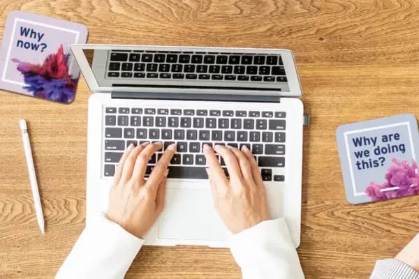 Photo of a laptop computer on a wooden desk with printed cards on either side reading 