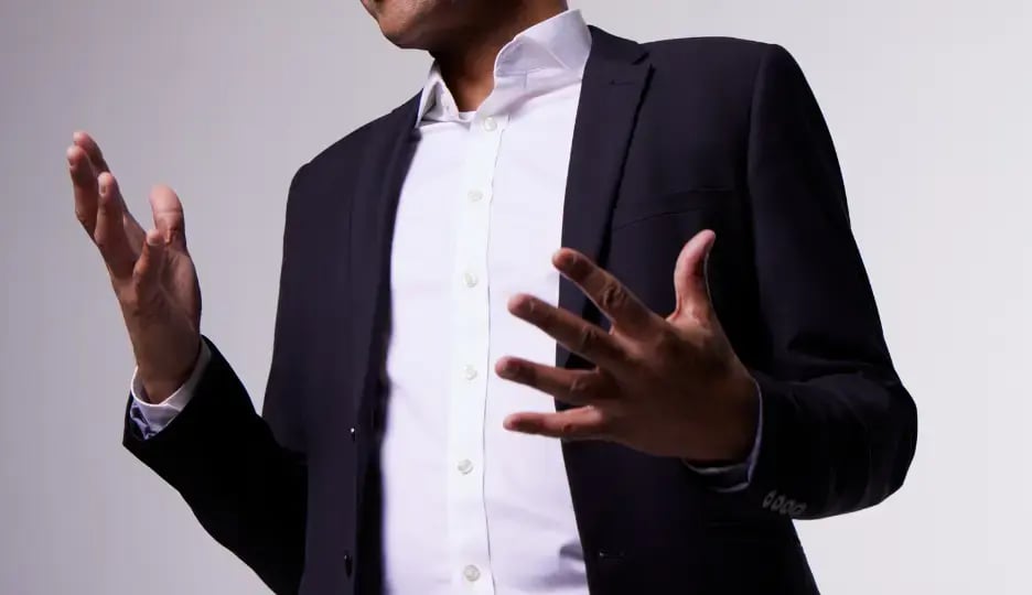 A man with a white shirt and black jacket, talking with his hands