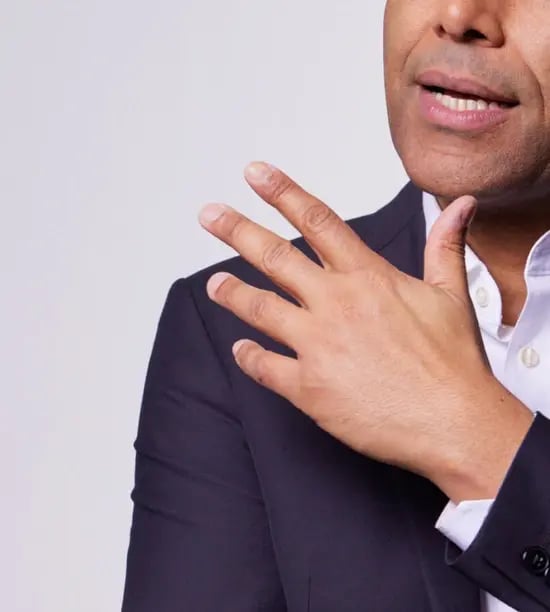 Photo of a man with dark complexion wearing a grey-navy suit and gesturing over his shoulder