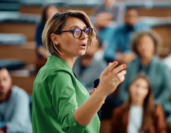 Photo of a woman in a green shirt giving a talk or lecture to a group
