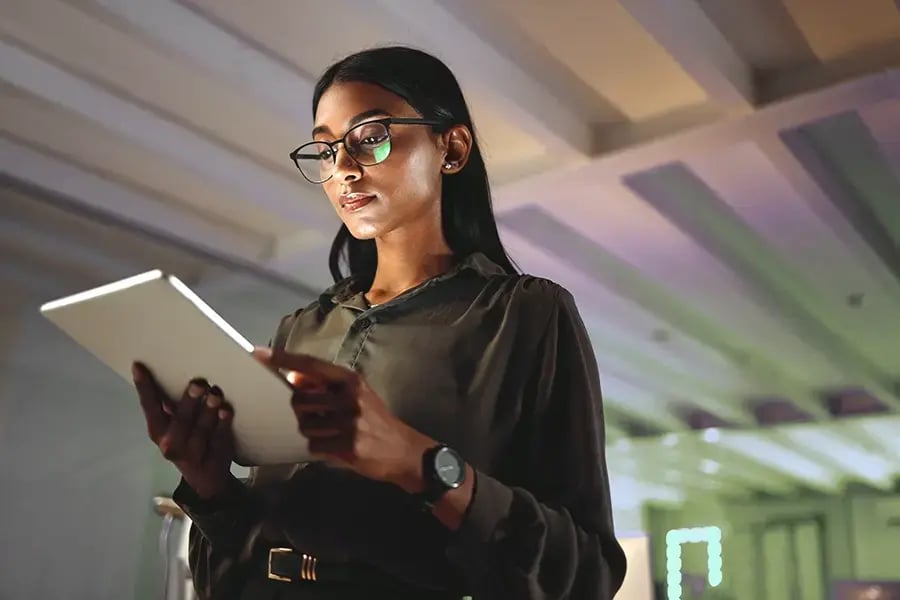 Photo of a woman wearing glasses and staring down at a tablet she's holding