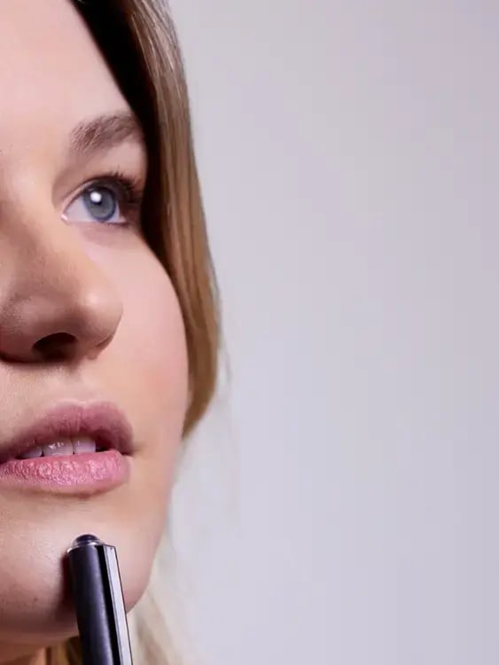 Photo of a white woman's face with a pen to her chin and an expression of reflection
