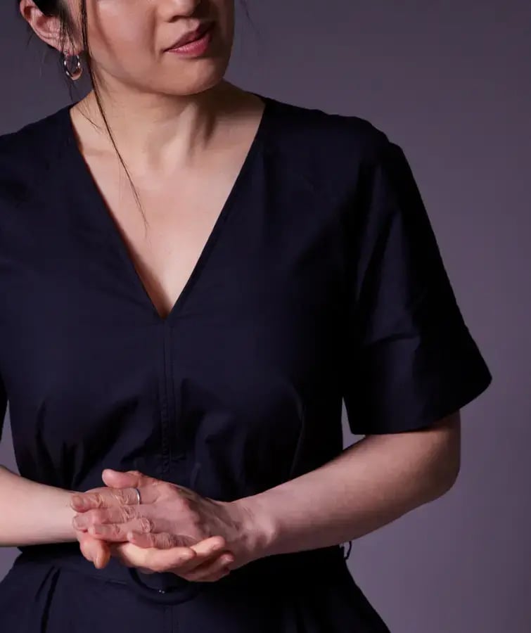 Photo of a woman in a dark dress standing with her hands held together